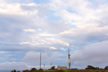 building with telecommunication antennas on hill with dramatic cloud sky in background. communications concept.