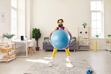 Happy young man doing exercise with a fit ball and having fun during sport workout at home