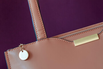 Part of leather handbag of beige color with metal details close-up, dark violet background. No name, no logo