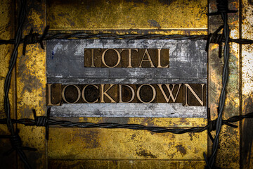 Total Lockdown text formed with real authentic typeset letters on vintage textured silver grunge copper and gold background with lined with barbed wire