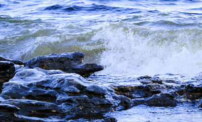 waves run onto the shore and crash against the rocks, creating many splashes and splashes near the shore. river surf in stormy weather near a stone pebble coast with foamy splashing waves.