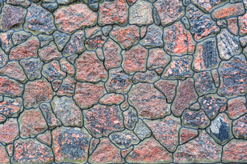 Fragment of a stone wall made of natural stone in red tones. The stones are of various sizes and shapes. There is a decorative black outline. Background. Texture.