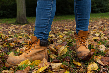 Fototapeta premium Detail picture of two yellow boots on the grass surrounded by leaves that have fallen down from the trees during the autumn season