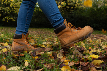 Detail picture of two yellow boots on the grass surrounded by leaves that have fallen down from the trees during the autumn season