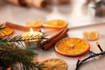 Cinnamon sticks, dried orange and lemon, green fir-tree, candles and colorful lights on the table. Christmas decoration, festive mood.
