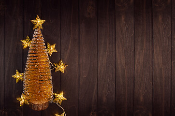 Rich christmas background - golden christmas tree, with stars garland glowing warm light on dark brown wood plank, top view, border.