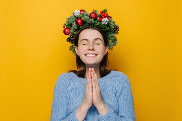 Cute young girl in Christmas wreath hands folded in prayer beg about something good, dressed in...
