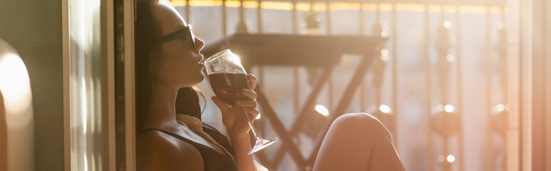 brunette woman in sunglasses drinking wine on balcony, horizontal banner