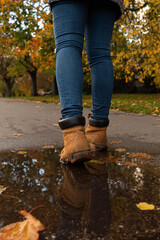 Detail picture of two yellow boots with its reflection on a puddle and yellow leaves in the background