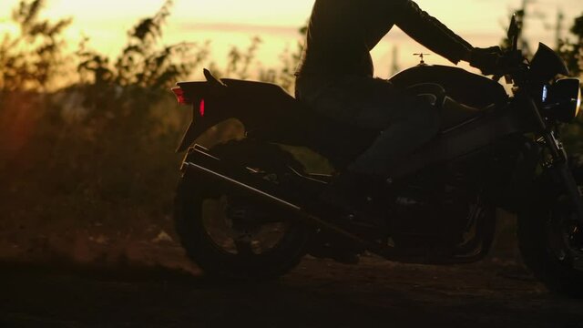 Close-up Wheel of Powerful Sport Motorcycle Starting Movement. Modern Bike Start Move. Dry Ground or Dust Flying Around Slow Mo. Concept of Motorsport or Active Lifestyle. Biker at Sunset Side view 4k