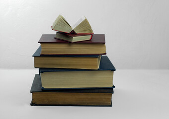 A stack of old thick hardcover books.On top of it is a small open book.Gray background .Selective focus.