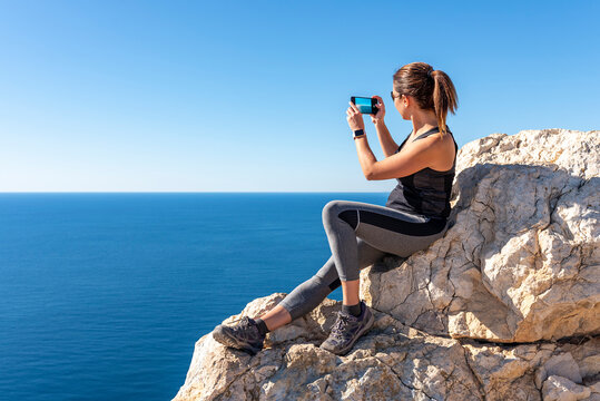Woman taking pictures with her smartphone to the landscape, in nature from the Peñon de Ifach in Calpe