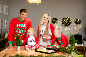 Happy family of four mom, dad, son and baby daughter drink Christmas cocoa in the kitchen