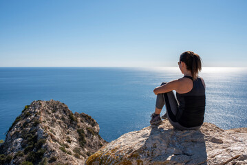 Naklejka na ściany i meble Woman with sportswear sitting on some rocks observing the landscape of the Mediterranean Sea