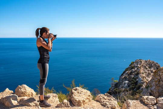 Woman taking pictures with her camera to the landscape, in nature from the Peñon de Ifach in Calpe