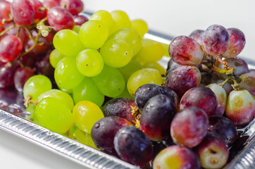Three types of green, red and black grapes on a silver tray