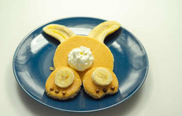 Creative meal for a child, pancake with banana, chocolate and whipped cream in a rabbit shape