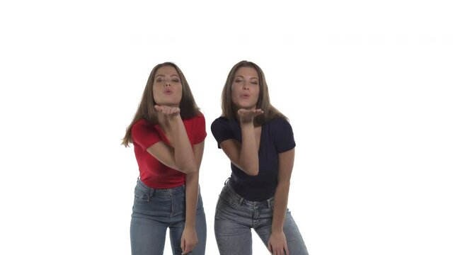 Sexy Caucasian twin sisters turning to each other and sending air kiss to camera. Isolated on white background.