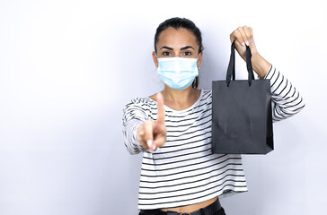 Young beautiful woman holding a black shopping bag wearing a medical mask to protect herself from the coronavirus . Black Friday