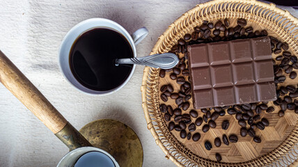Photo of a bar of chocolate, coffee beans, coffee in a turk. Freshly brewed coffee in a cup. View from above. Flat lay