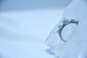 Close-up silver ring frozen into ice on white background, selective focus