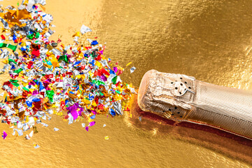 Bottle of champagne with gold glitter, confetti and space for text on gold background, top view.