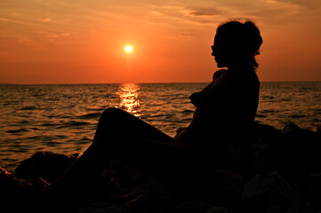 Romantic girl sitting on the pier near the water at sunset