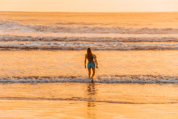 Fototapeta na wymiar Female surfer on the beach at the sunset in Balneario Comboriu state of Santa Catarina