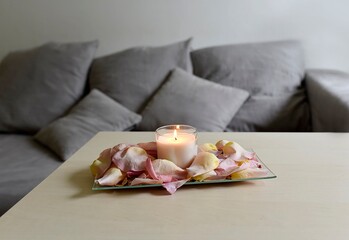 Fototapeta na wymiar burning candle in rose petals in the living room with a gray sofa