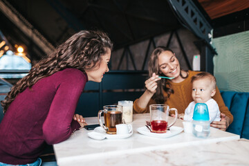 Two friends enjoying in cafe bar with cute little baby boy.