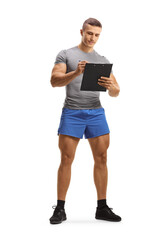 Full length portrait of a muscular young man in sportswear writing on a clipboard