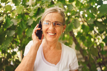 Elderly senior happy woman in prescription eyeglasses speaks smartphone outdoor