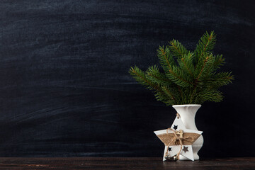 Fototapeta premium A vase with Christmas tree branches and a handmade star decoration against a chalkboard. The concept of a merry Christmas. Copy space.