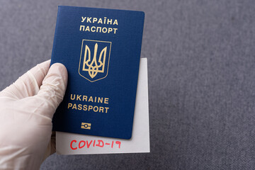Hand in medical glove holding passport with Covid-19 note. Coronavirus disease outbreak. Travelling in epidemic period. Passport border control and quarantine of infected tourists