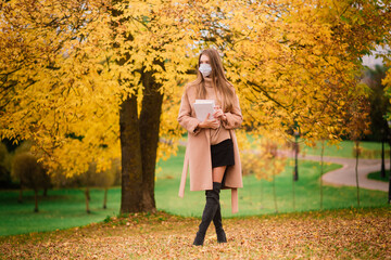 Portrait of a beautiful adult young woman on the background of autumn in park in medical face mask