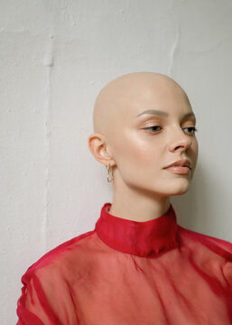 Portrait of a young bald girl in a red blouse. Minimalist studio portrait