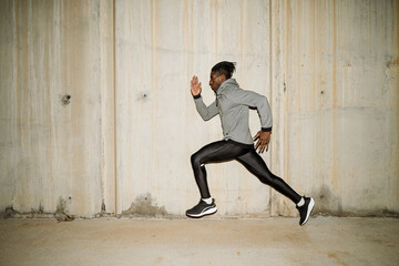 Solitary ethnic determined runner training along street in evening