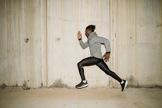 Solitary ethnic determined runner training along street in evening