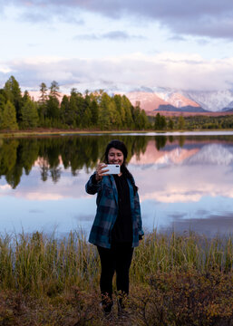 young girl traveler stands on the background of a lake and mountains and talks via video link with her friends