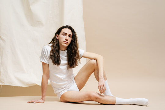 Androgynous guy sitting near fabric