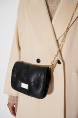 Girl in a beige coat with a black leather handbag on a golden chain. Luxury fashion background. Vertical photo.