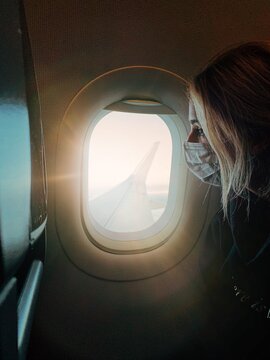 Girl Wearing Mask Looking Out Window of Airplane