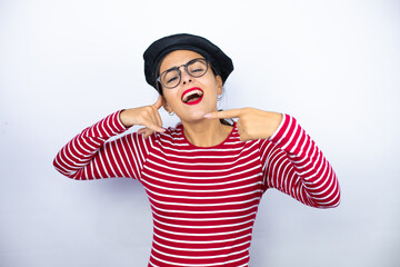 Young beautiful brunette woman wearing french beret and glasses over white background doing the “call me” gesture with her hands.