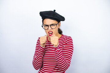 Young beautiful brunette woman wearing french beret and glasses over white background Punching fist to fight, aggressive and angry attack, threat and violence