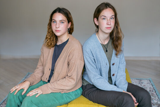two similar girls are equally sitting on a yellow sofa