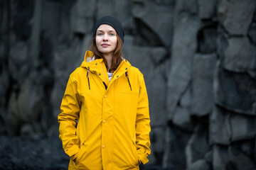 Woman in a yellow jacket on a background of basalt rocks, Iceland