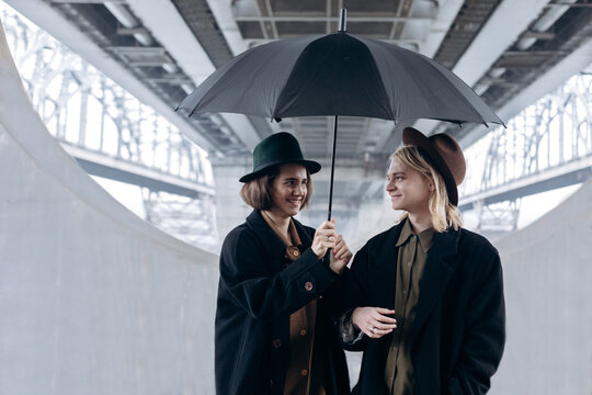 two stylish guys in hats and coats are standing under the bridge