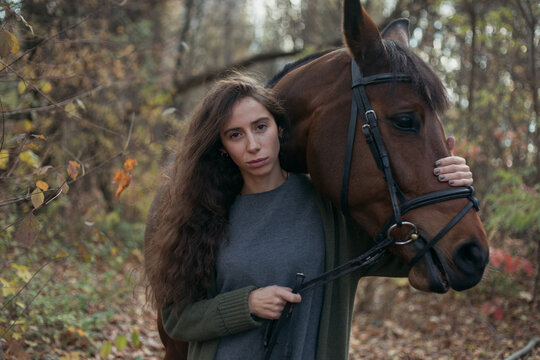photo of a dark-skinned girl with long curly hair with her brown horse in nature