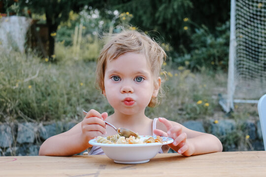 Little Girl Eating Pasta In A Garden In Summer