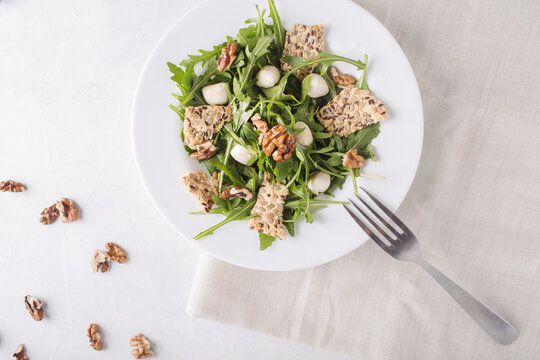 Diet salad with arugula, mozzarella and walnuts on a light gray background